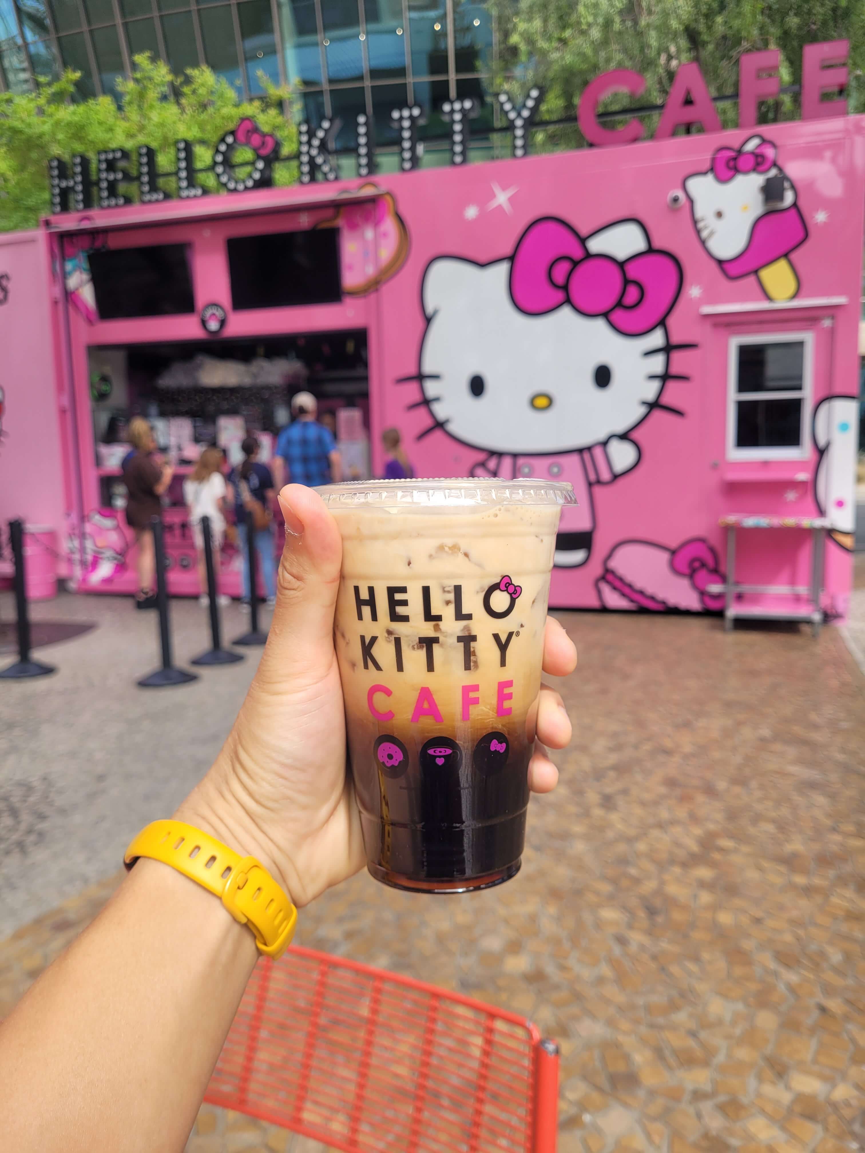 Iced coffee held up in front of the pink Hello Kitty Cafe truck